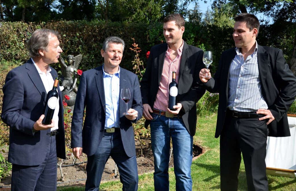 The Massenez Family Wine Estate team, including Dominique Massenez, Serge Dubs Best Sommelier of the World, Jean Massenez and Master Winemaker Stephane Geneste, celebrating with fine wine in a vineyard setting.